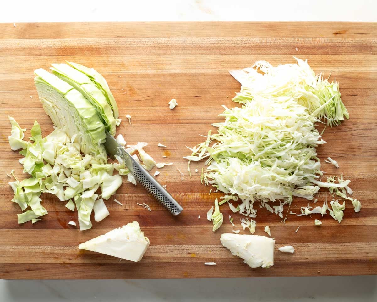 Two piles of green cabbage, one is thinly sliced and one is roughly chopped. 