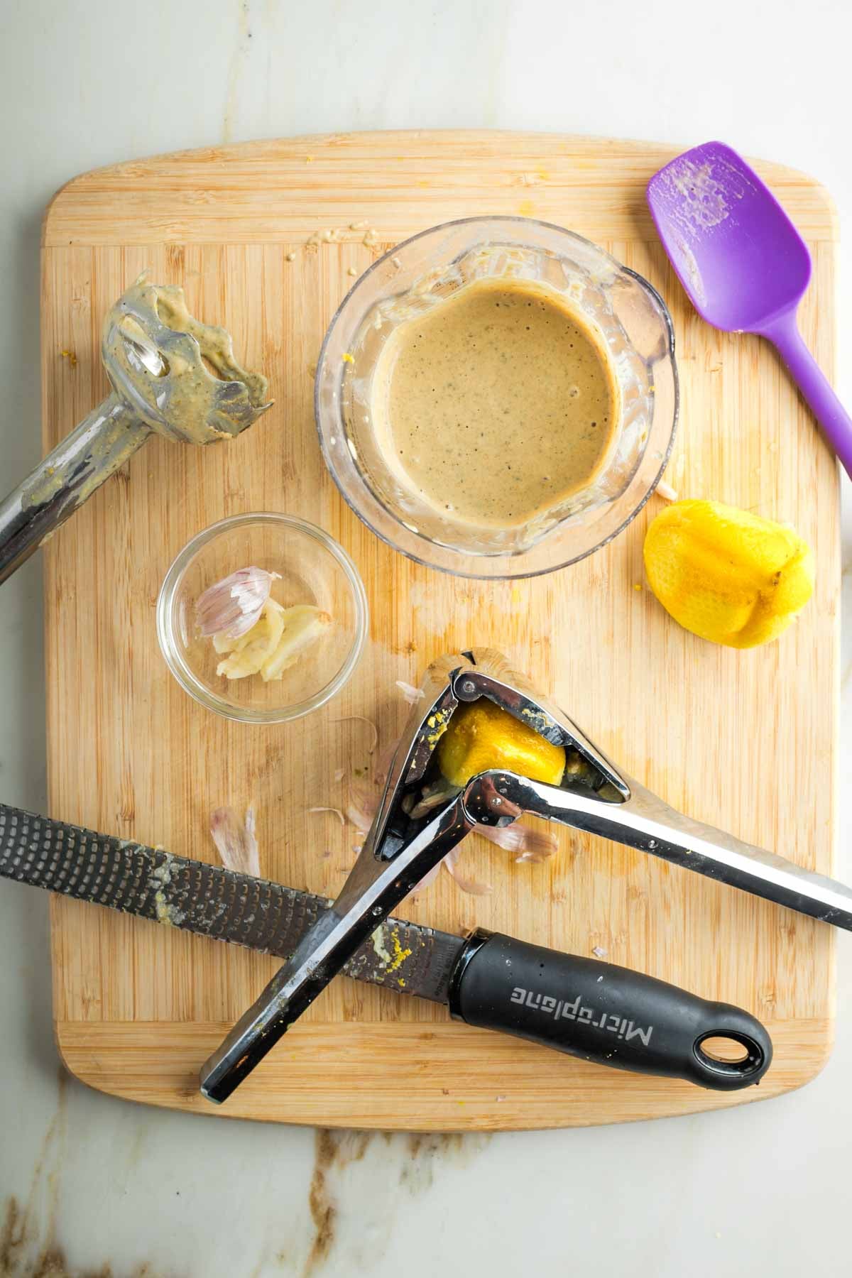 Wooden board, with tools to make caesar dressing; immersion blender, microplane, juicer, spatula. 