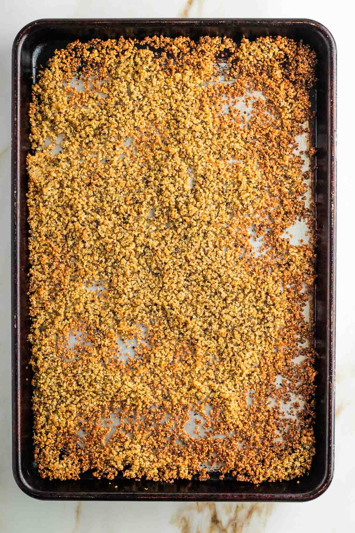 Golden brown crispy quinoa on a rimmed baking sheet. 