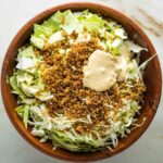 Chopped cabbage, crispy quinoa and vegan caesar dressing in a large wooden bowl.