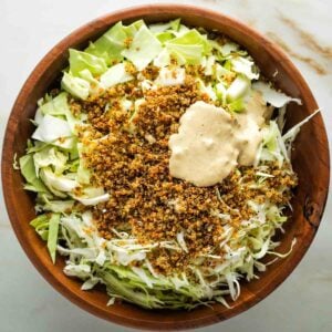 Chopped cabbage, crispy quinoa and vegan caesar dressing in a large wooden bowl.