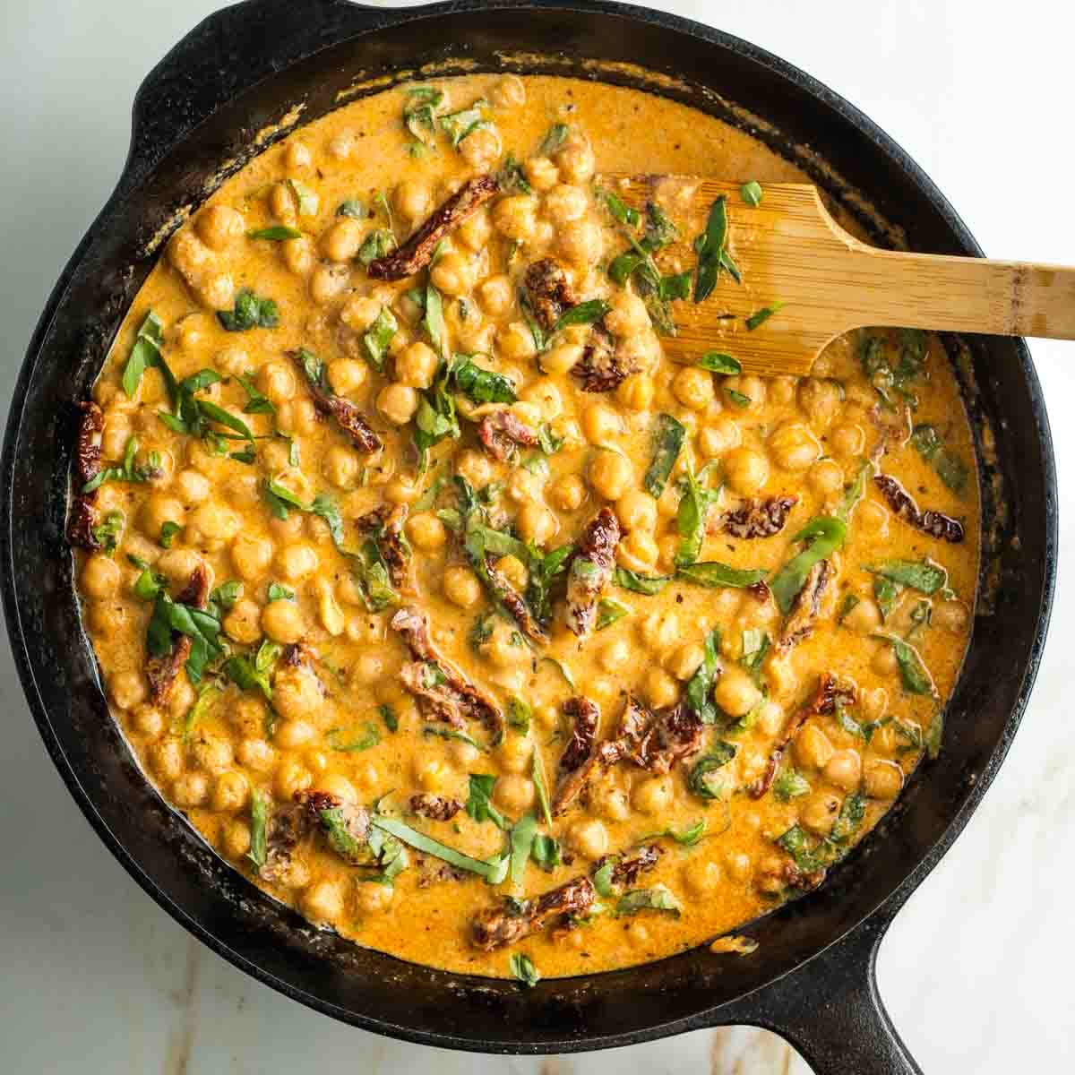 Cast iron skillet with chickpeas, sun dried tomatoes and fresh basil in a creamy orange sauce.