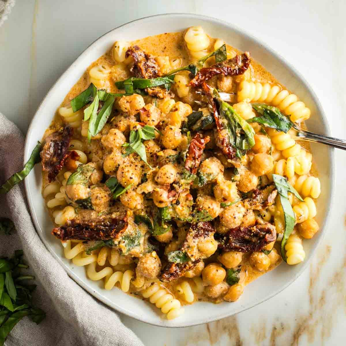 Creamy chickpeas and sun dried tomatoes served over pasta with fresh basil as garnich.