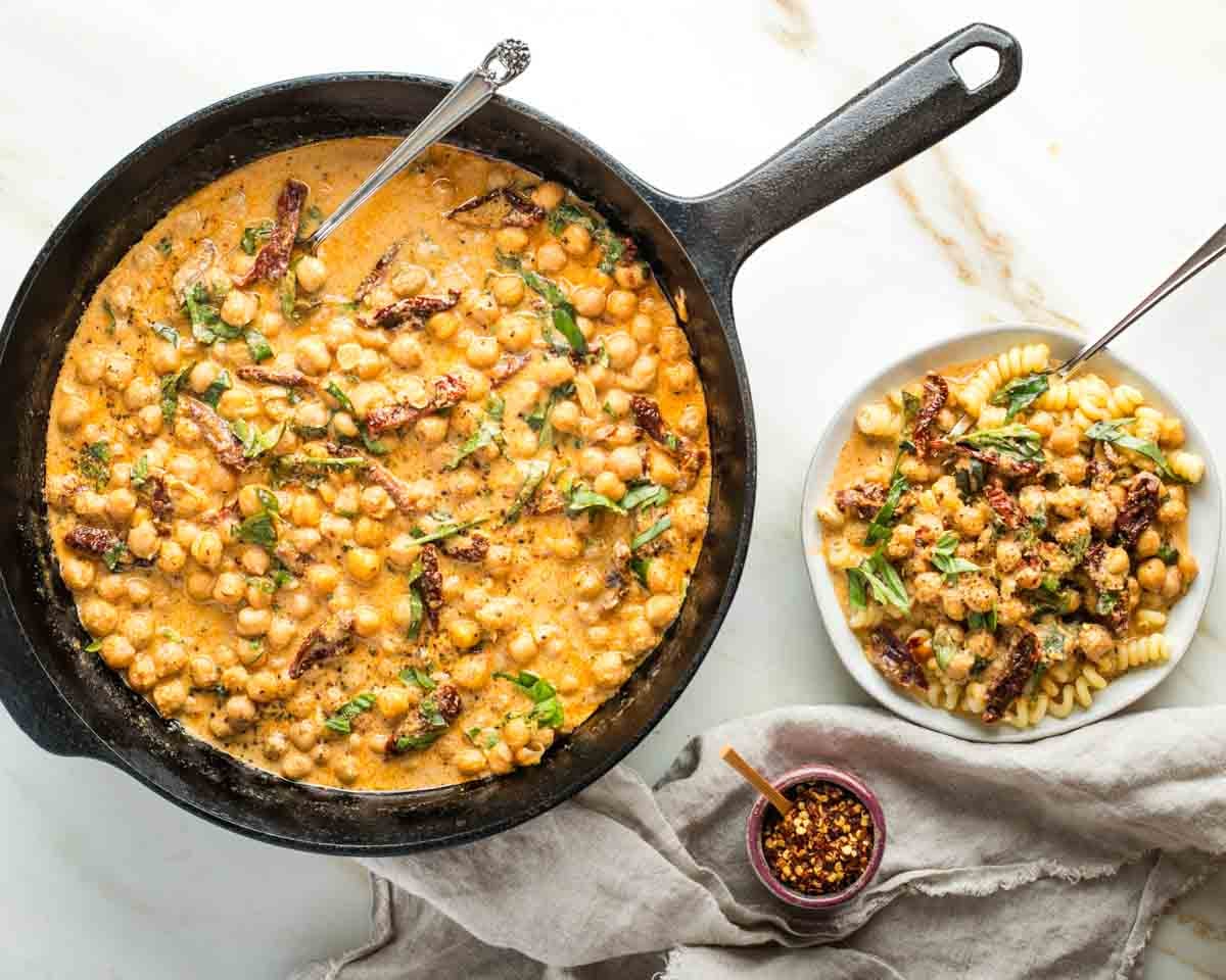 Skillet of marry me chickpeas and then served over pasta on a plate. 