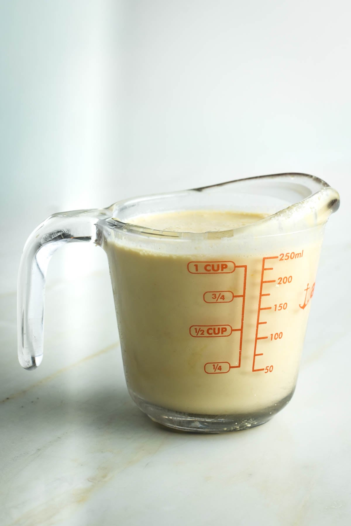 Glass measuring cup filled with creamy yellow sauce.
