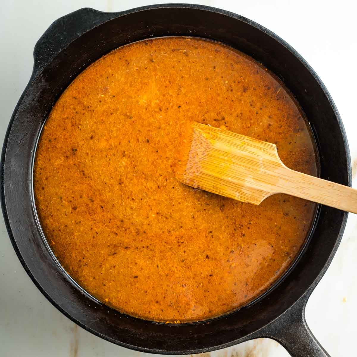 Stirring a light colored tomato sauce in a cast iron skillet