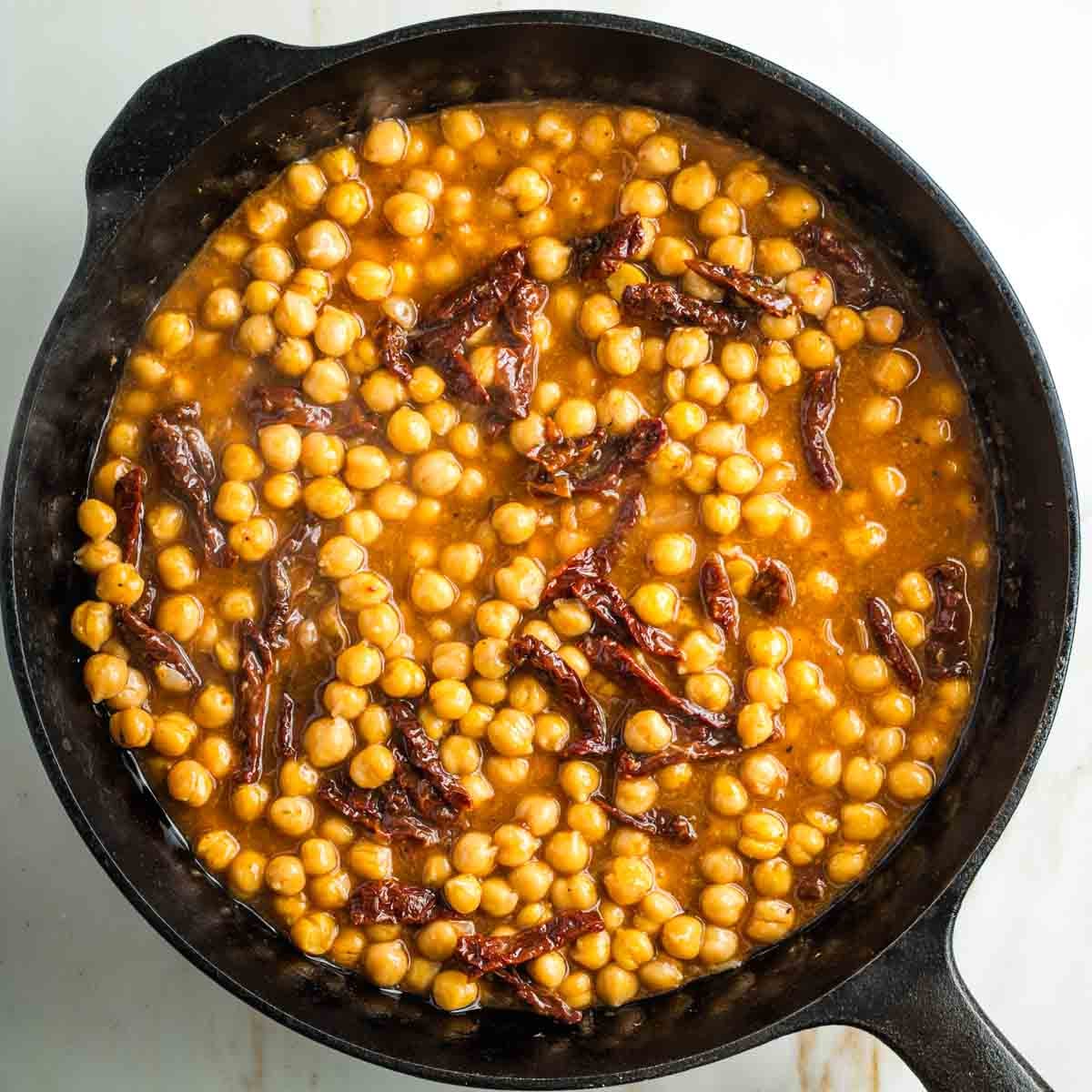 Cast iron skillet with chickpeas and sun dried tomatoes in a clear tomato based sacue.