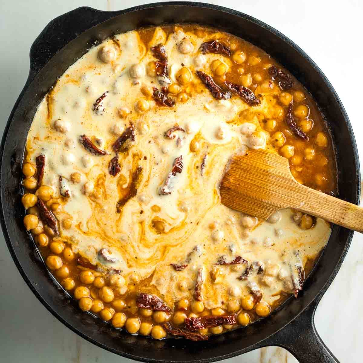 Cream mixing into a tomato chickpea and sun dried tomato skillet.