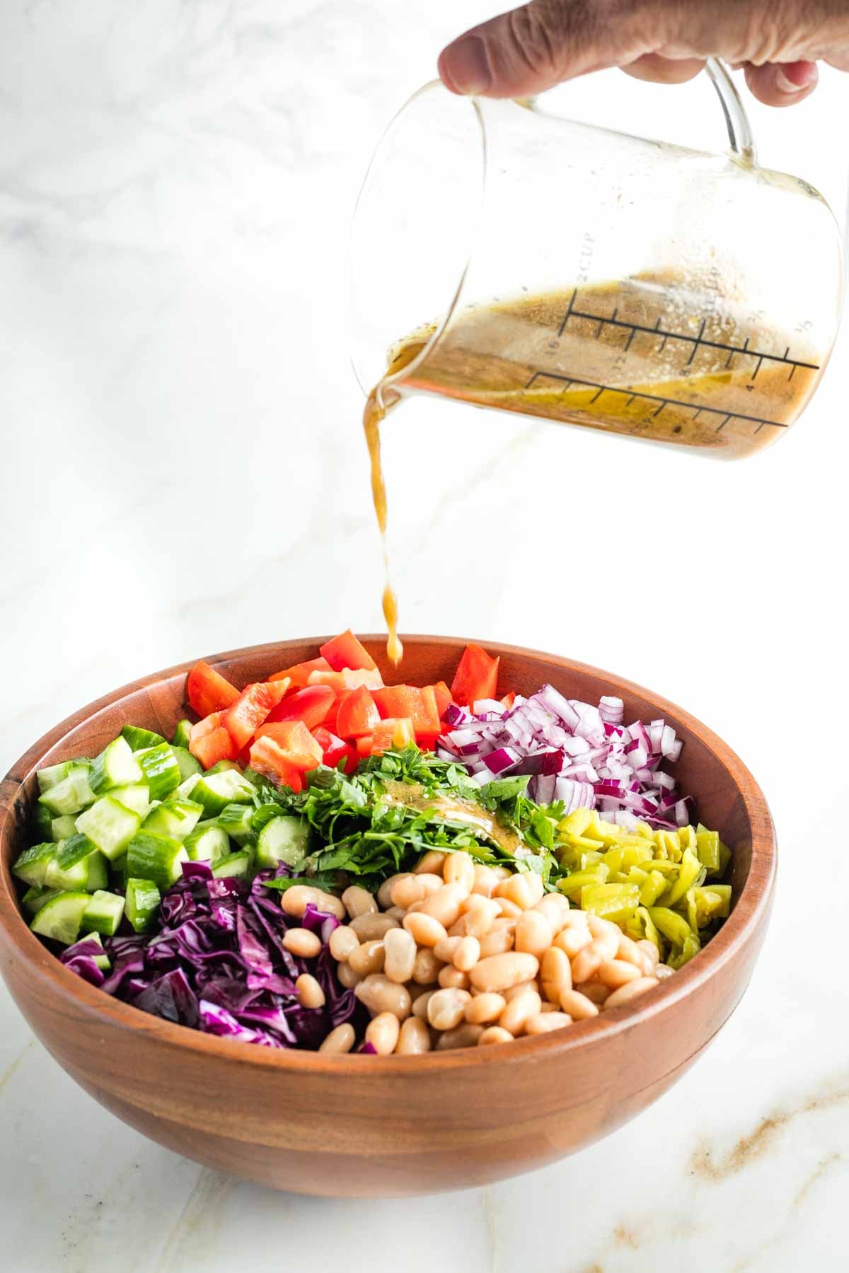 Pouring dressing onto a pasta salad with colorful chopped vegetables. 