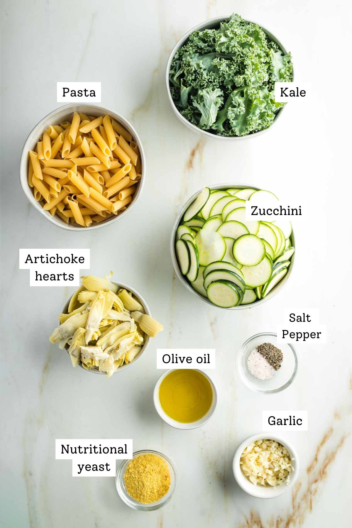 Labeled ingredients: pasta, kale, sliced zucchini, artichoke hearts, olive oil, salt, pepper, nutritional yeast and chopped garlic.