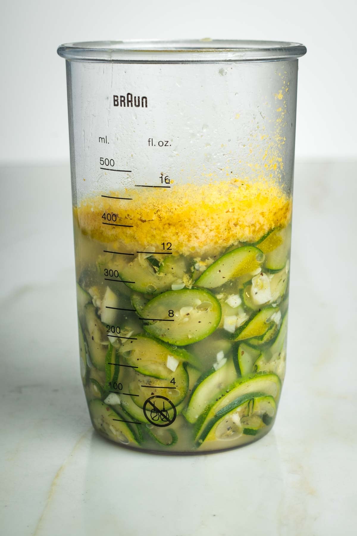 Tall cup with measuring markings on the side filled with sauteed zucchini rounds and nutritional yeast.