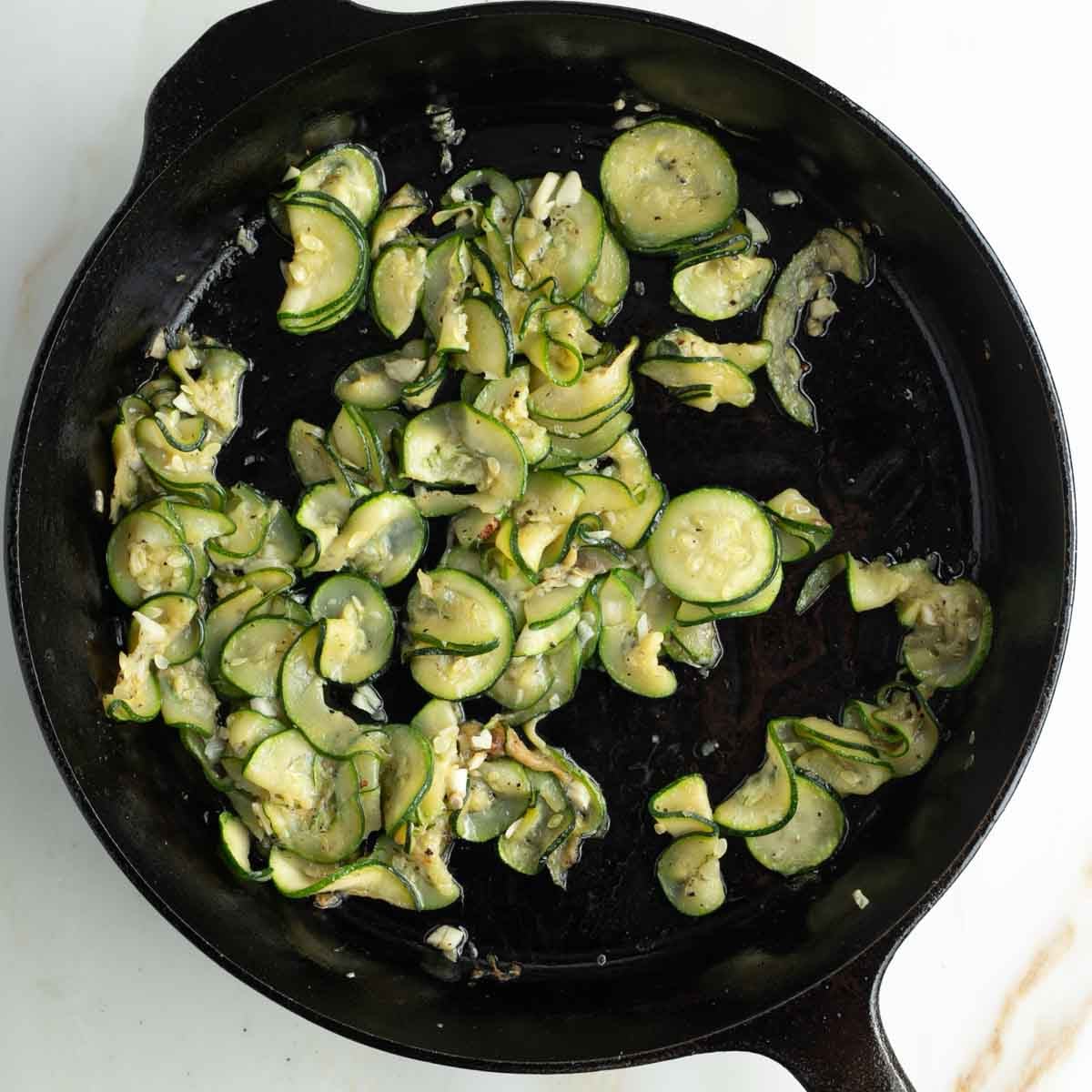 Cast iron skillet with a few sauteed zucchini rounds and chopped garlic.
