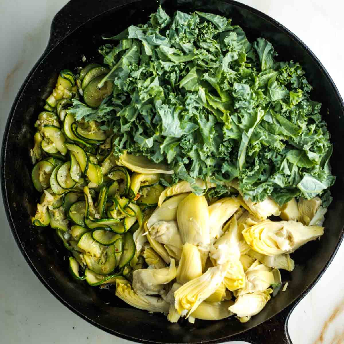 Skillet with sauteed zucchini and also kale and artichoke hearts.