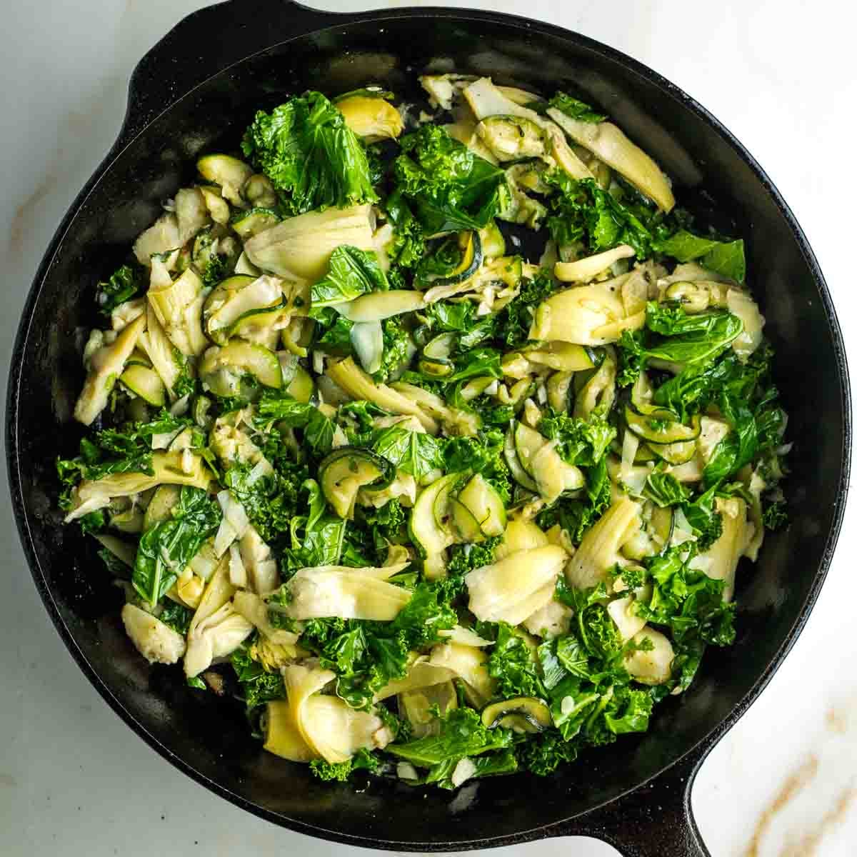 Skillet filled with kale, artichoke hearts and zucchini.