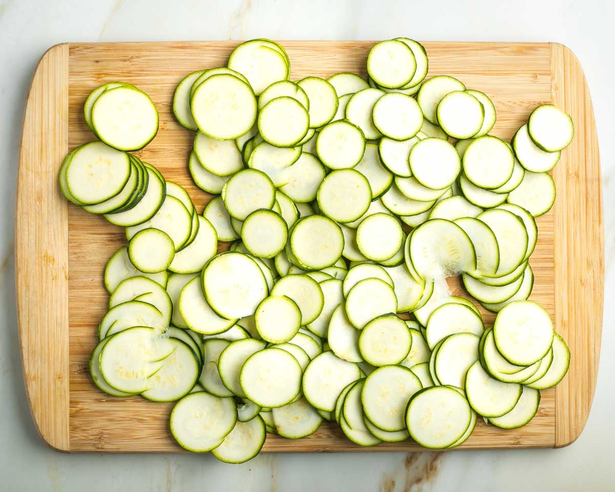 Thinly sliced zucchini rounds on a wooden board.