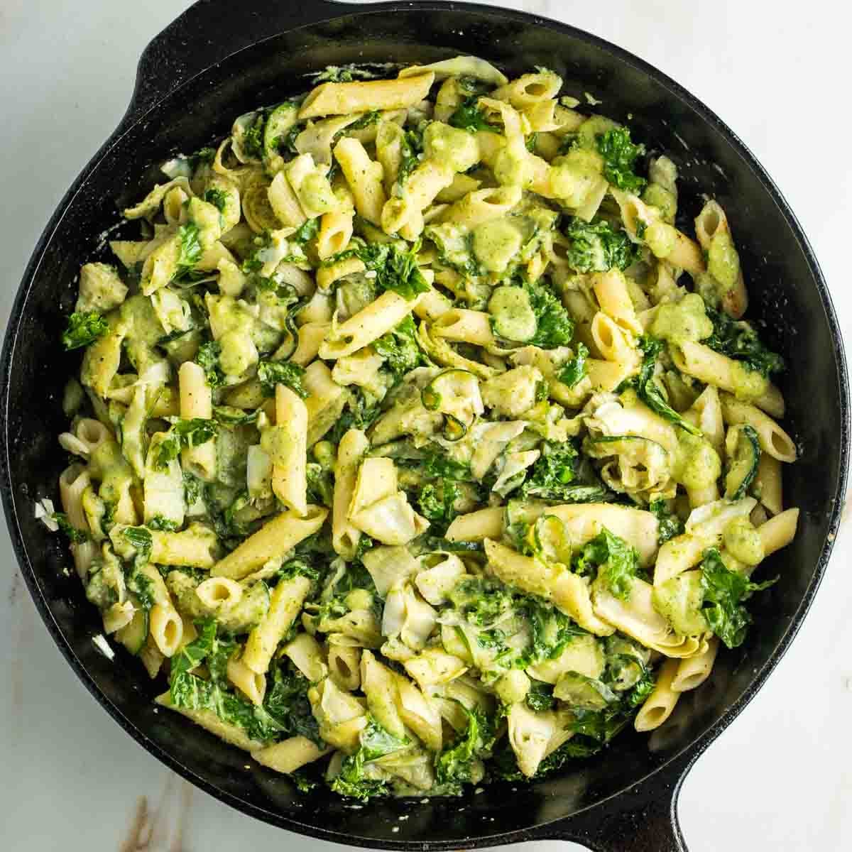 Skillet full of pasta with vegetables in a green sauce.