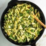 Cast iron skillet with ziti, zucchini, kale and artichoke hearts in a creamy green sauce.