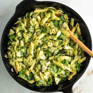 Cast iron skillet with ziti, zucchini, kale and artichoke hearts in a creamy green sauce.