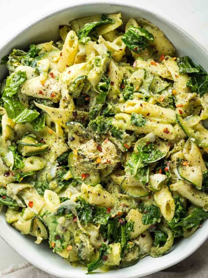 Bowl of pasta with kale, zucchini and artichoke hearts in a creamy green sauce.