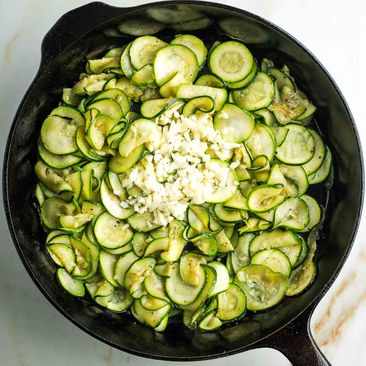 Sauteed zucchini rounds with a heap of chopped garlic in the middle of a cast iron skillet.