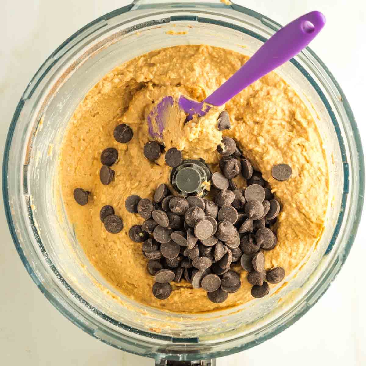 Stirring chocolate chips into cookie batter with a purple silicone spatula.