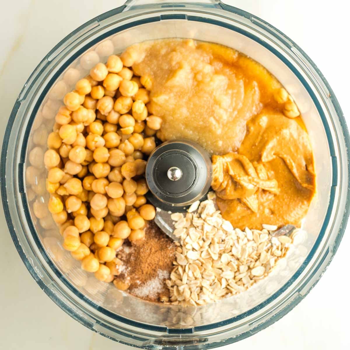Chickpeas, oats, applesauce, peanut butter and spices in the bowl of a food processor. 