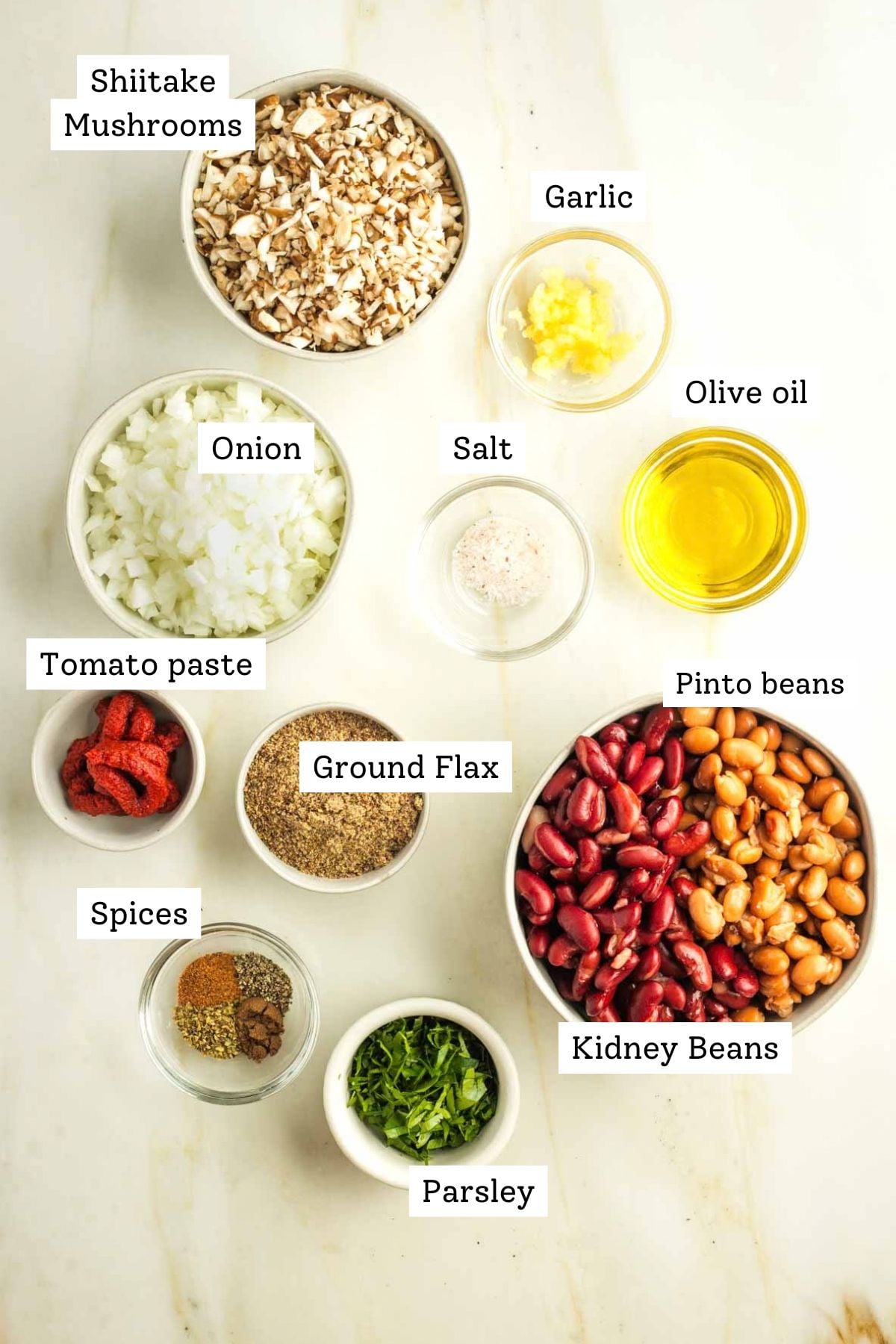 Labeled ingredients for vegan Swedish meatballs including diced mushrooms and onions, olive oil, two kinds of beans, ground flax, tomato paste, parsley and spices.