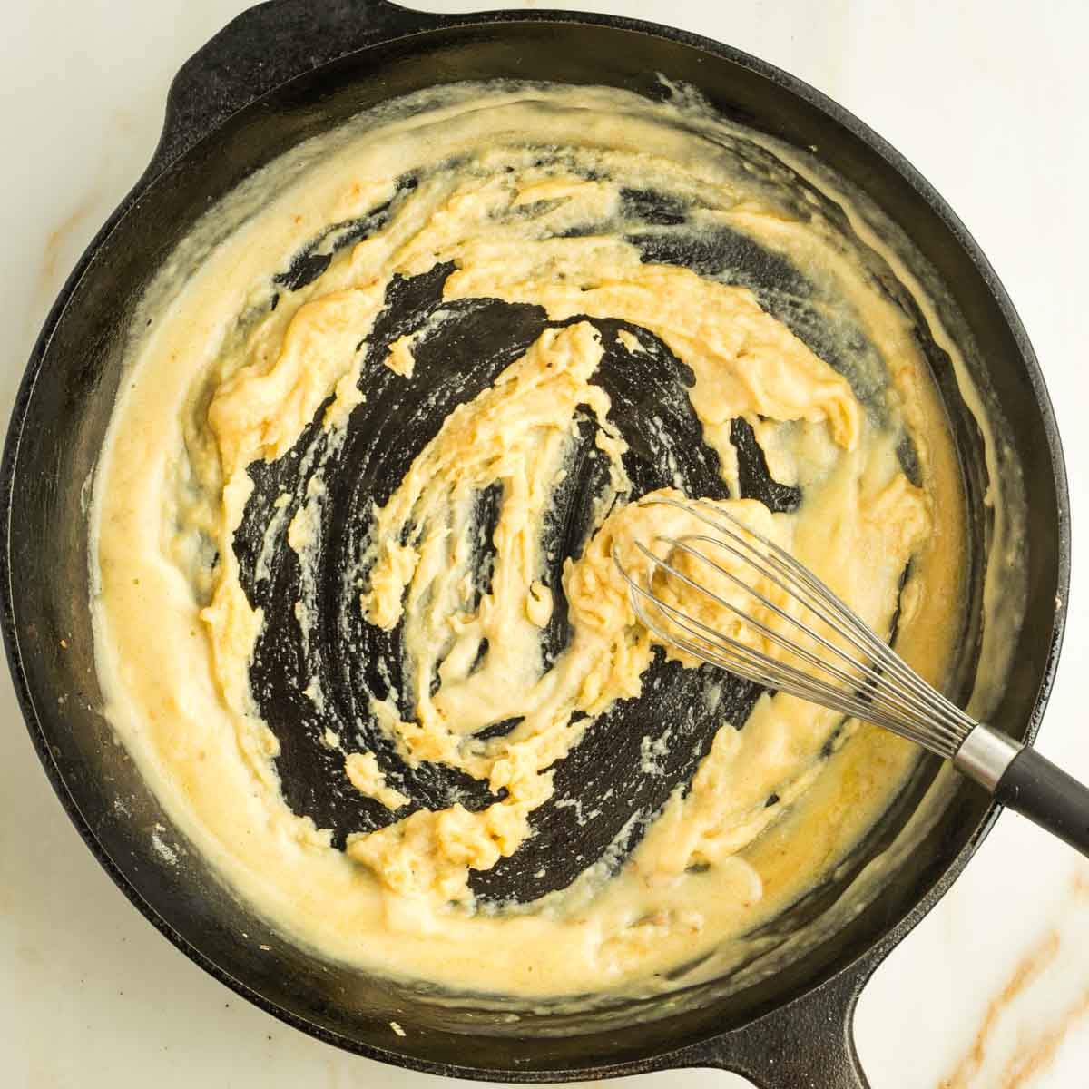 Whisking flour and olive oil into a paste in a cast iron skillet.