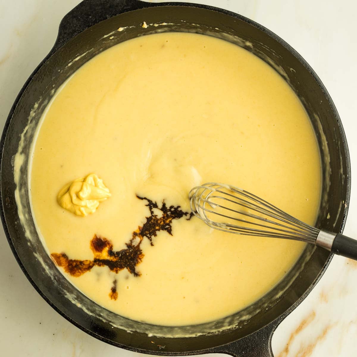 A bit of dijon mustard and some tamari added to a yellow creamy sauce in a cast iron skillet.
