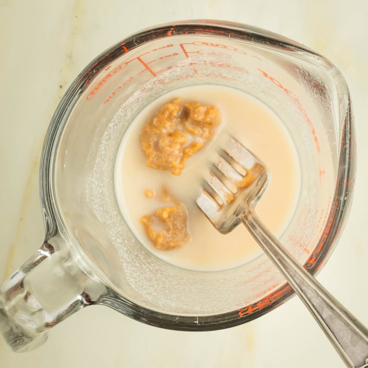 A fork mashing miso into some milk in a pyrex measuring cup.