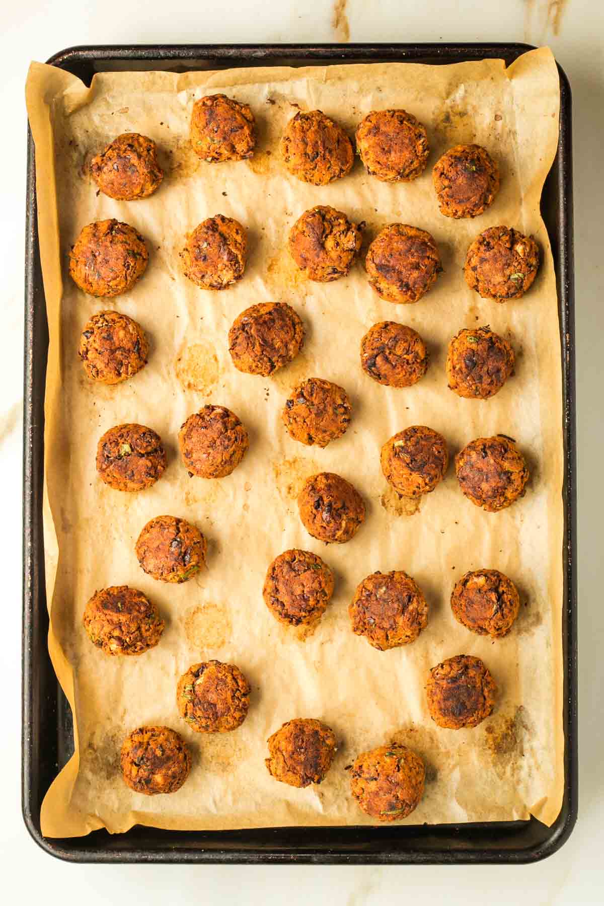 Baked vegan Swedish meatballs on a tray lined with parchment paper.