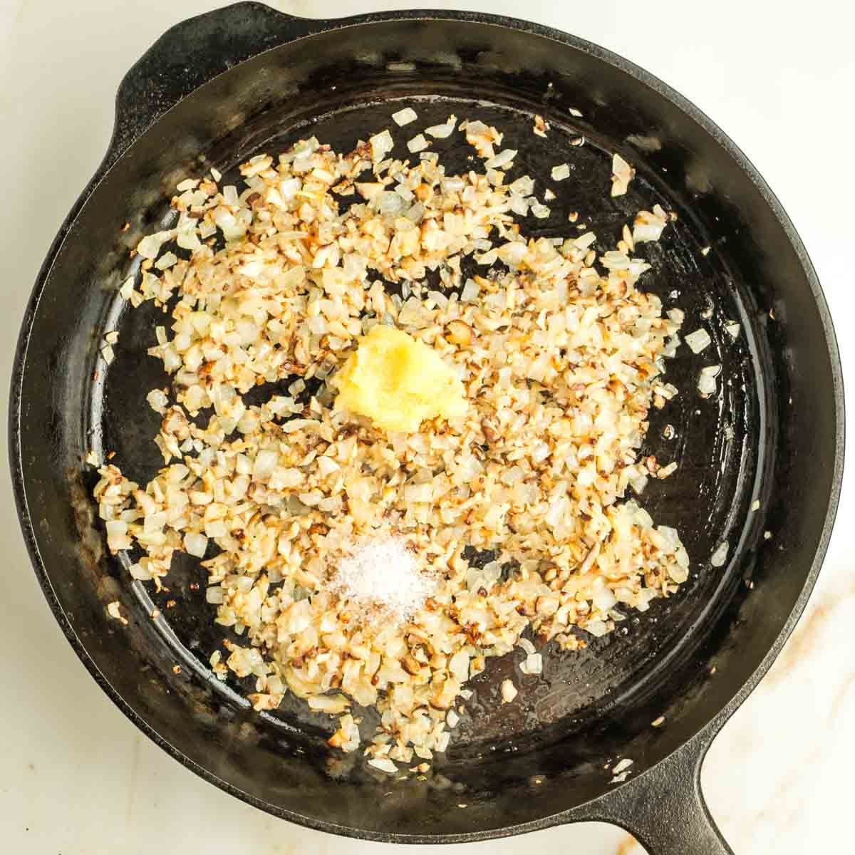 Sauteed onions and mushrooms in a cast iron skillet with grated garlic and salt on top.