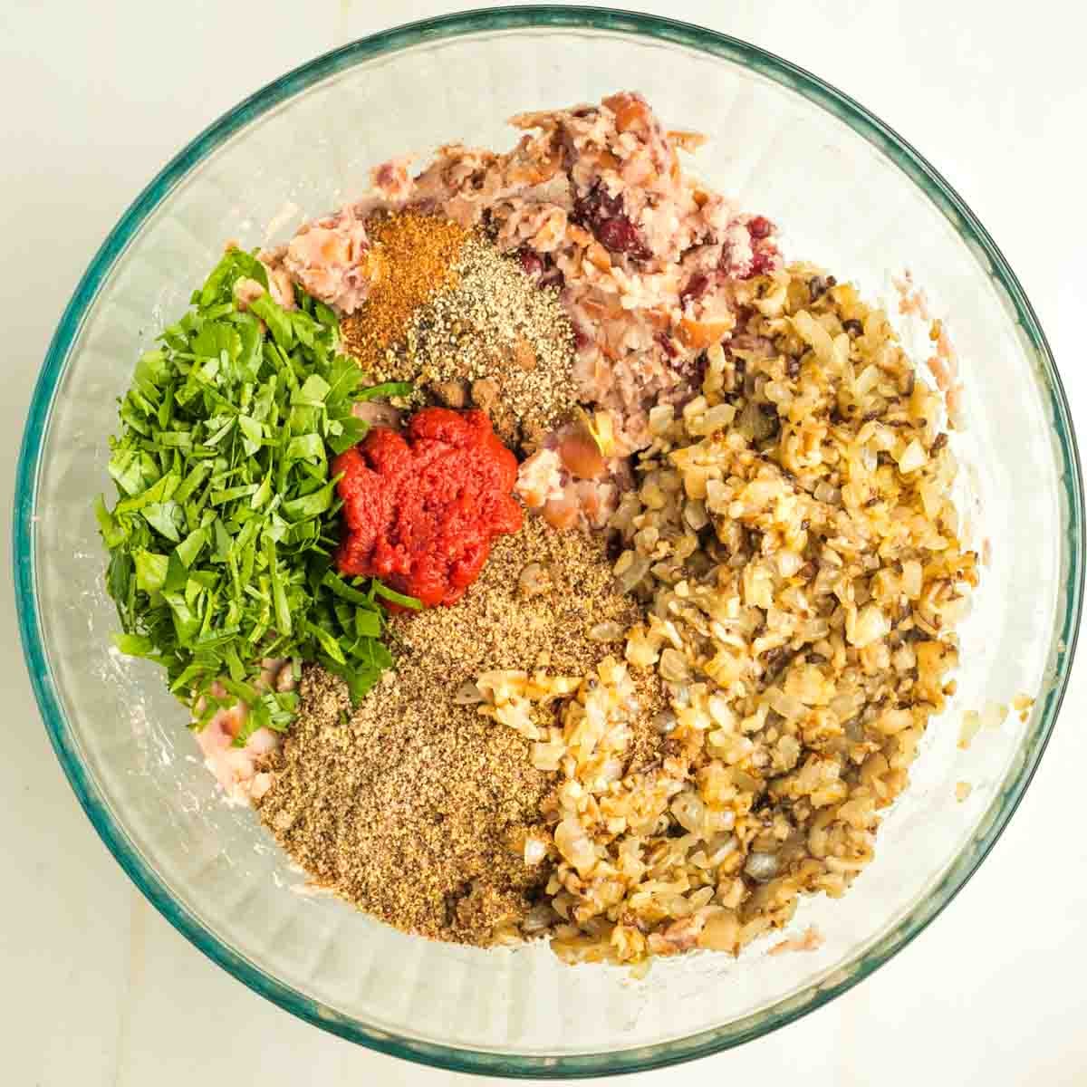 Mashed beans, sauteed mushrooms and onions, tomato paste, chopped parsley, ground flax and spices in a glass mixing bowl.