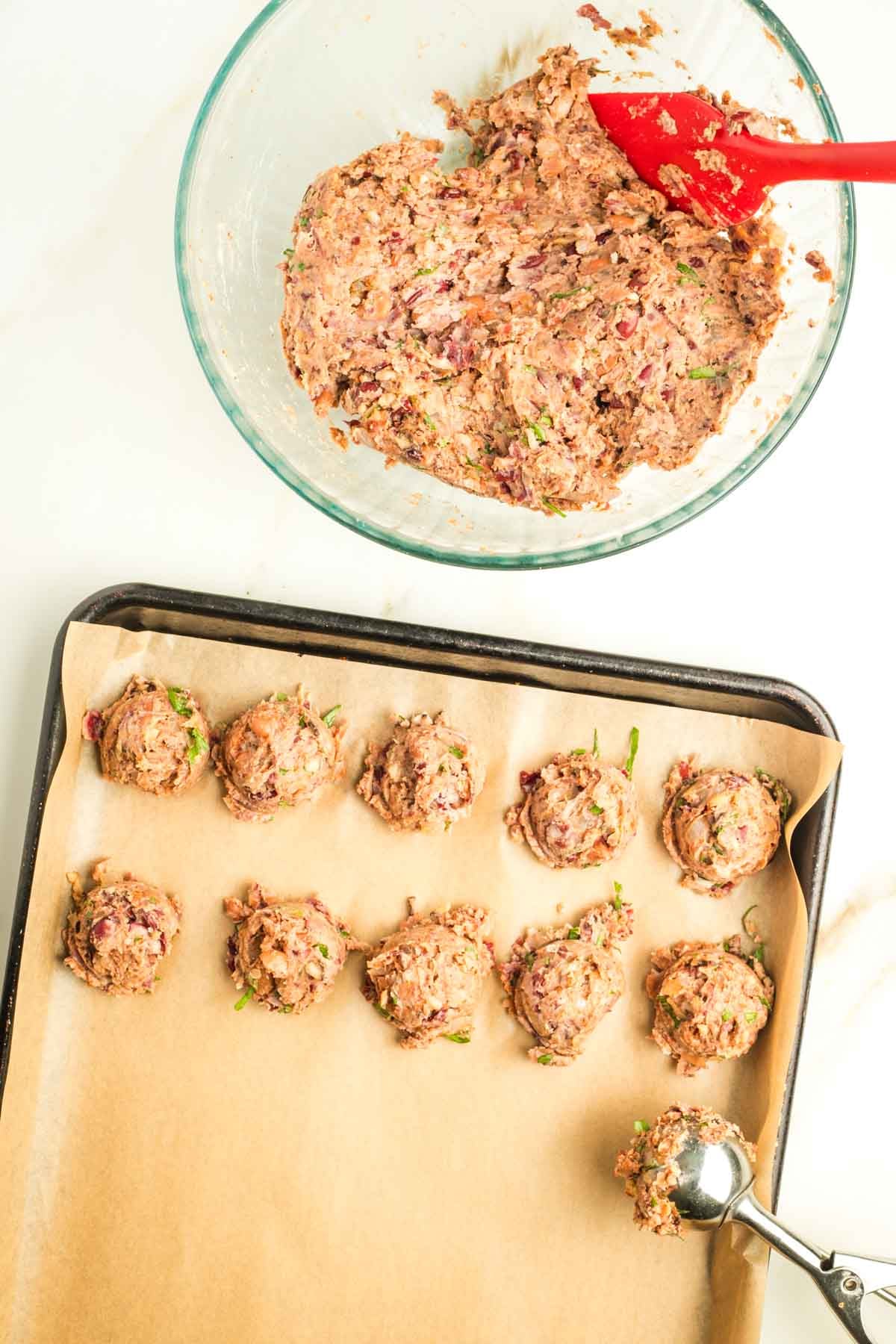 Small cookie scoop portioning out vegan Swedish meatballs from batter in a glass bowl.