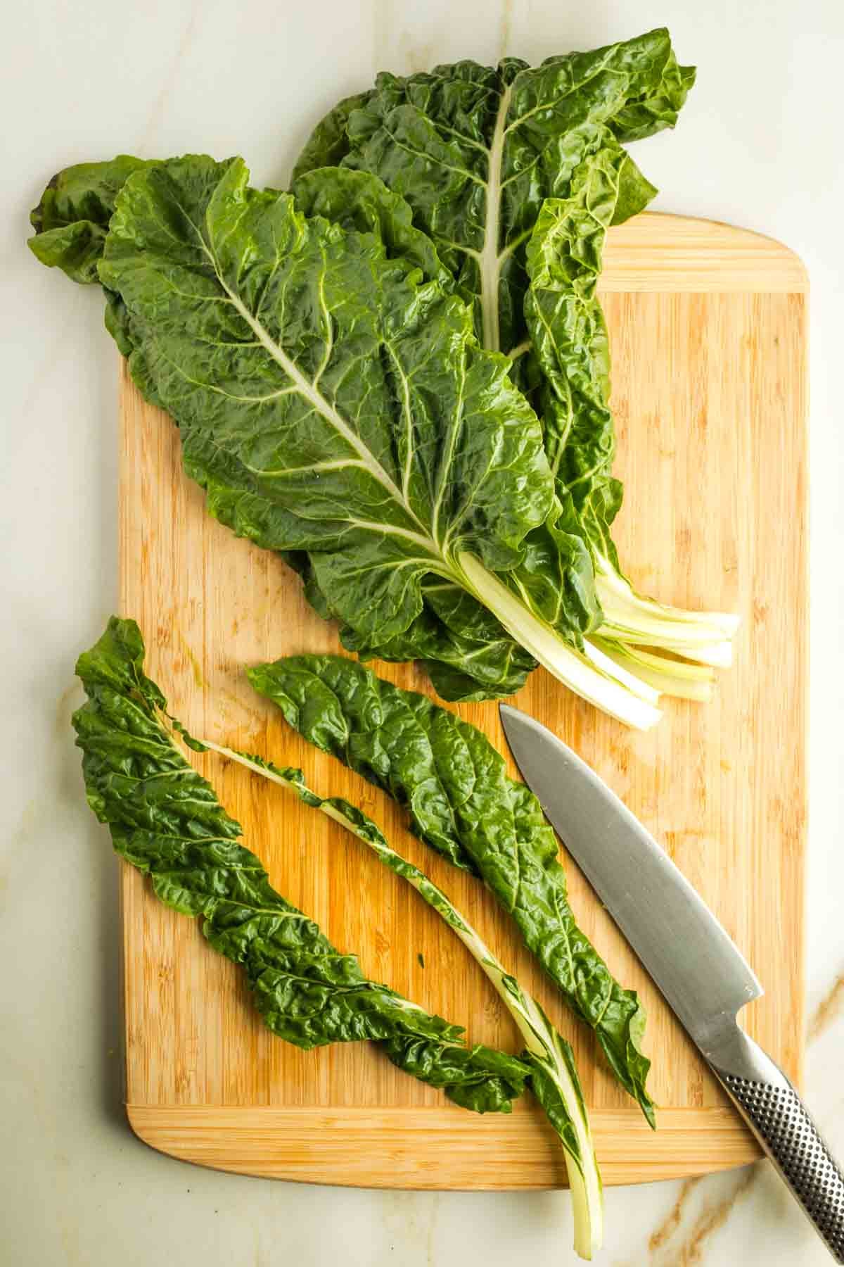 Knife cutting the greens from the stem on a Swiss chard leaf.