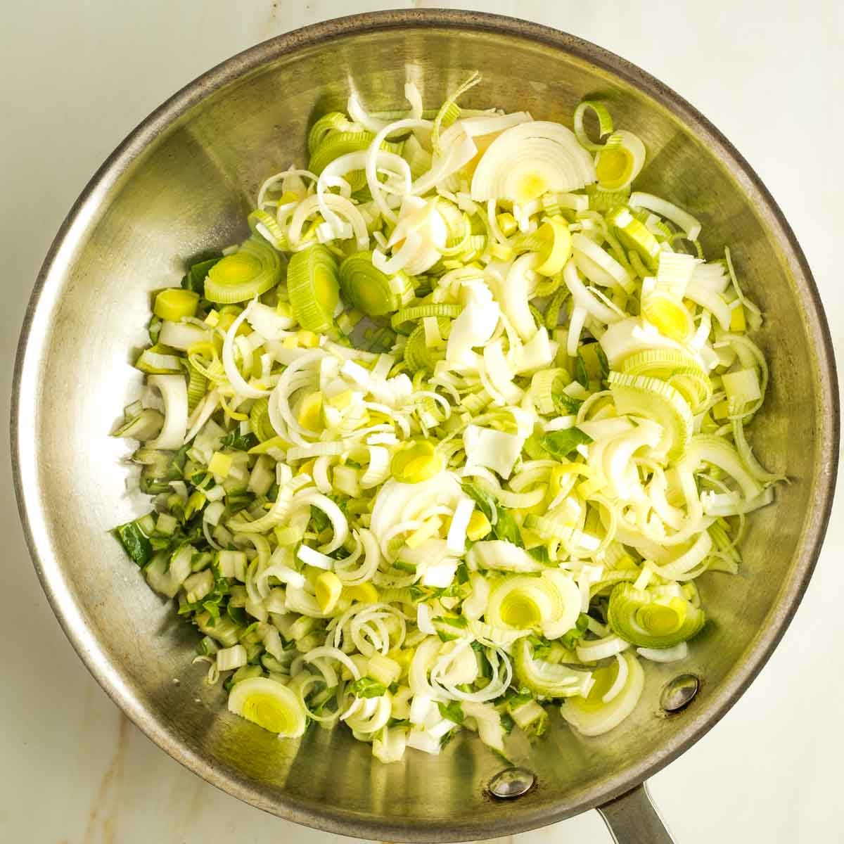 Thinly sliced leeks in a stainless steel fry pan.