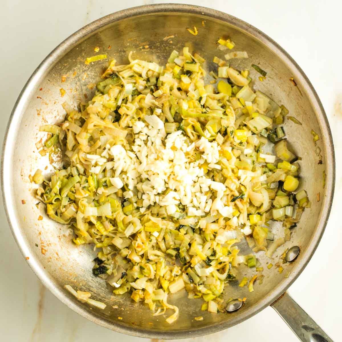 Stainless fry pan with sauteed leeks and chard stems and roughly chopped garlic added. 