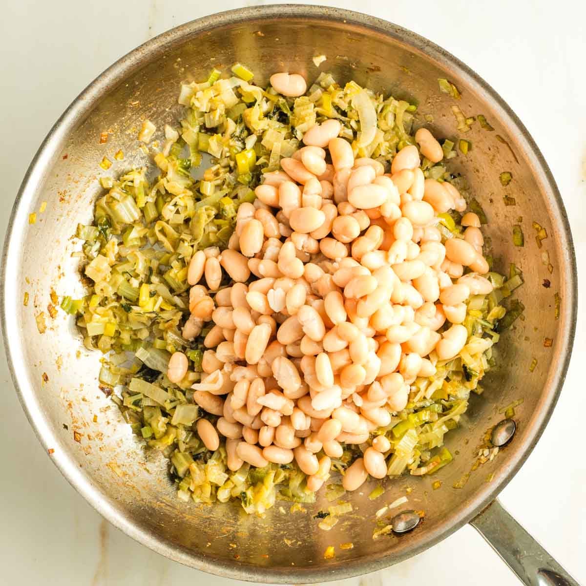 Cannellini beans added to a skillet of sauteed leeks and chard stems.