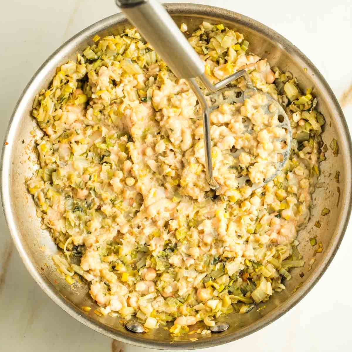 Mashing beans into a skillet of sauteed leeks and chard stems.