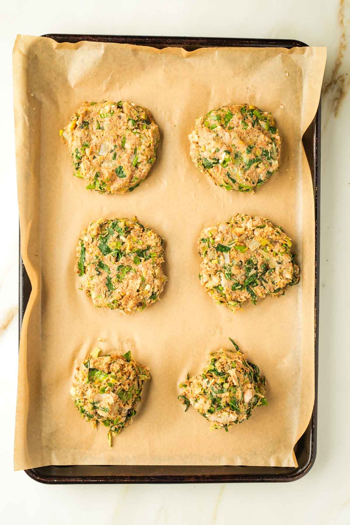 Balls of leek patty mixture dropped onto a baking sheet, some flattened into burgers.