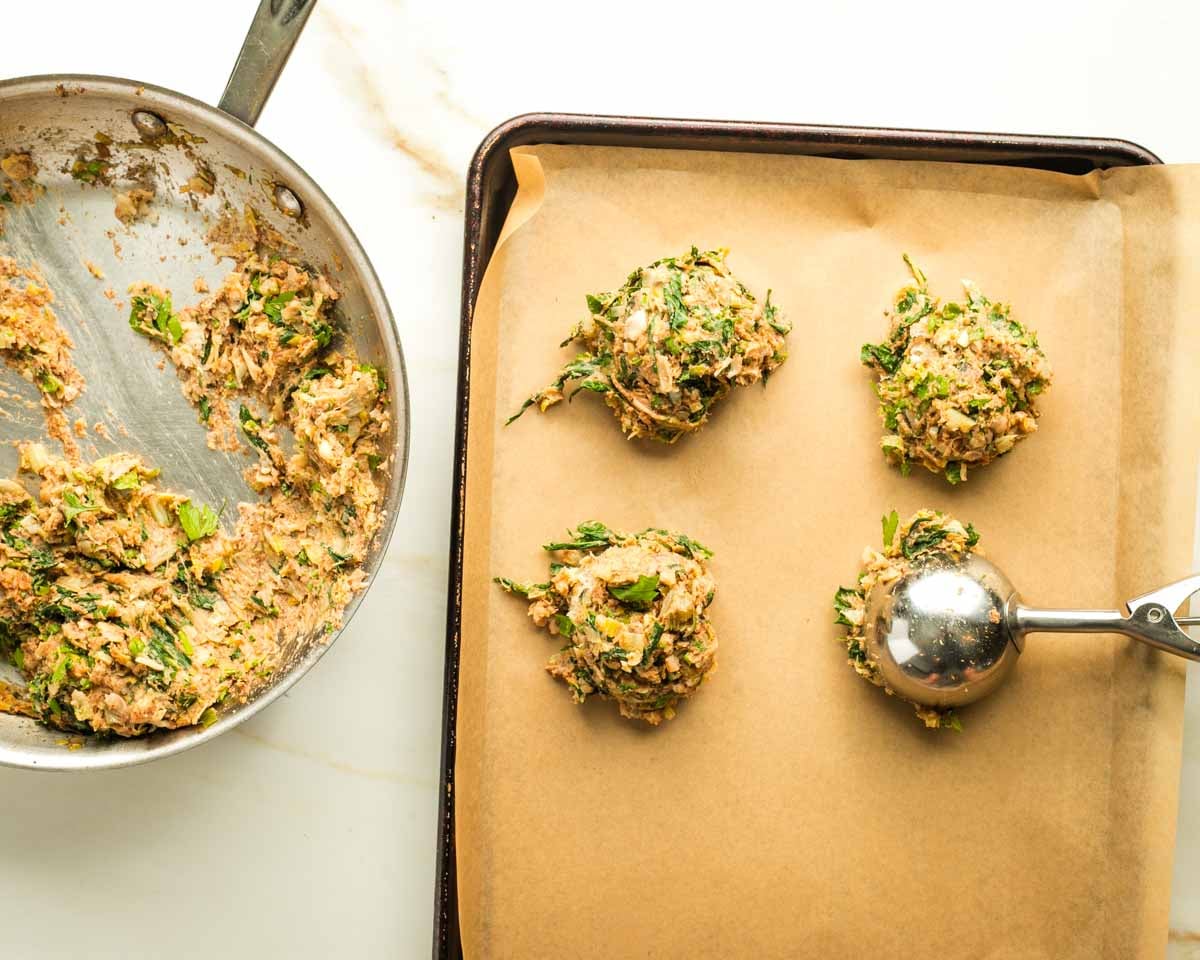 Scooping leek patty mixture from a bowl onto a baking sheet. 