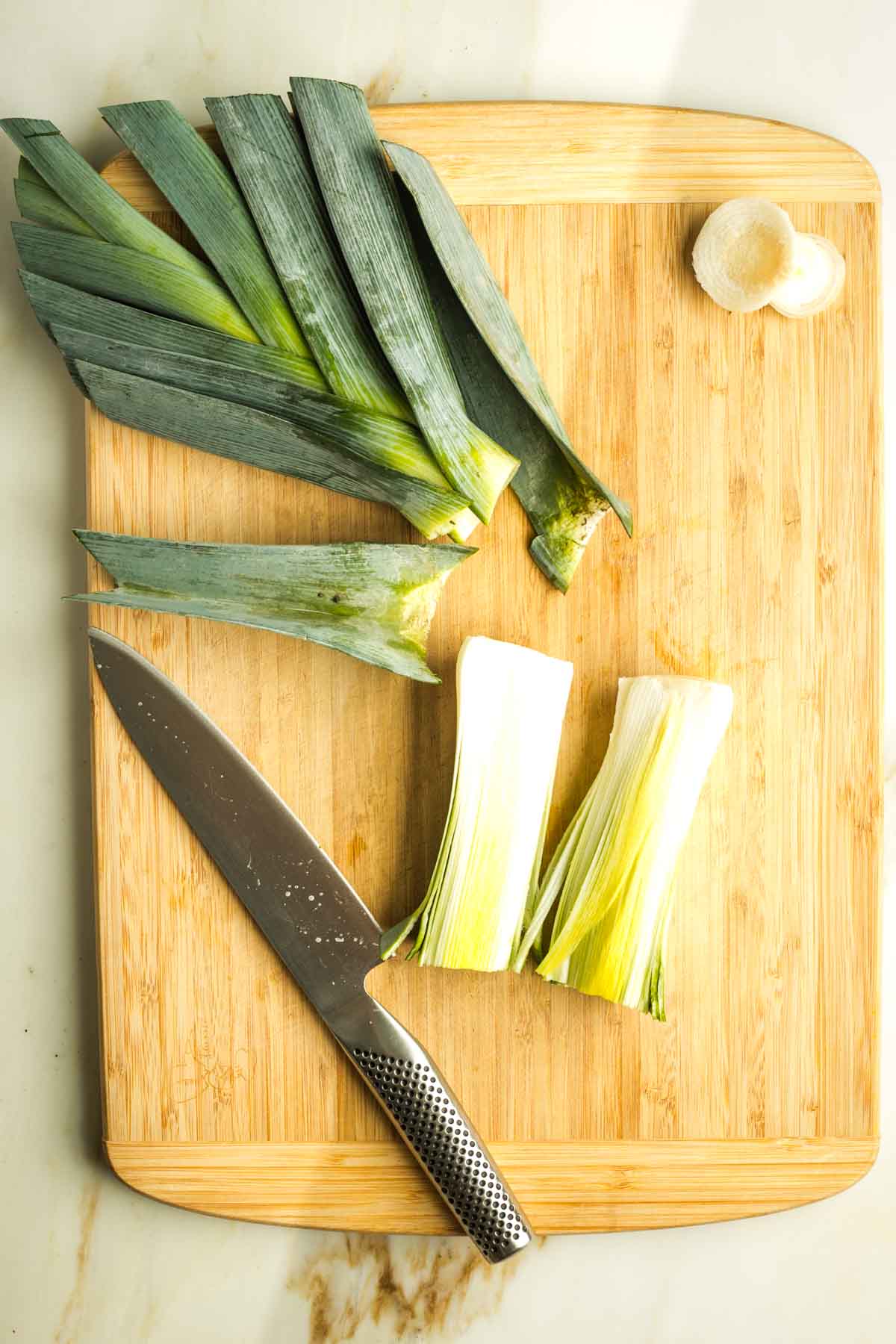Leeks on a cutting board with greens cut off, showing the dirt in between the layers and the white part cut in half lengthwise.