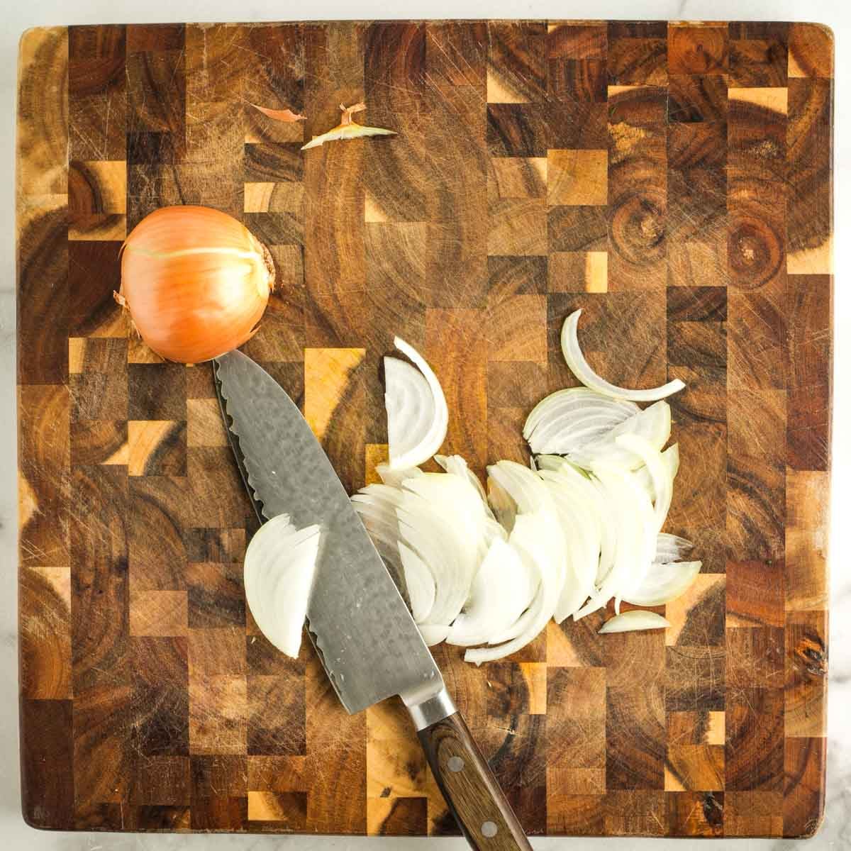 Thinly slicing an onion on a wooden board.