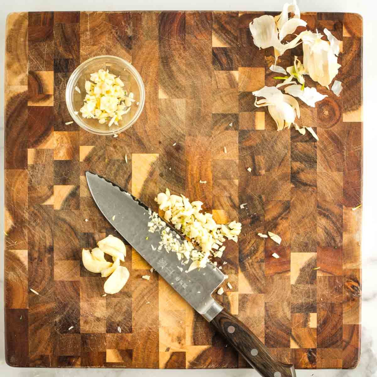Roughly chopping peeled garlic on a wooden board and putting it into a small glass dish.
