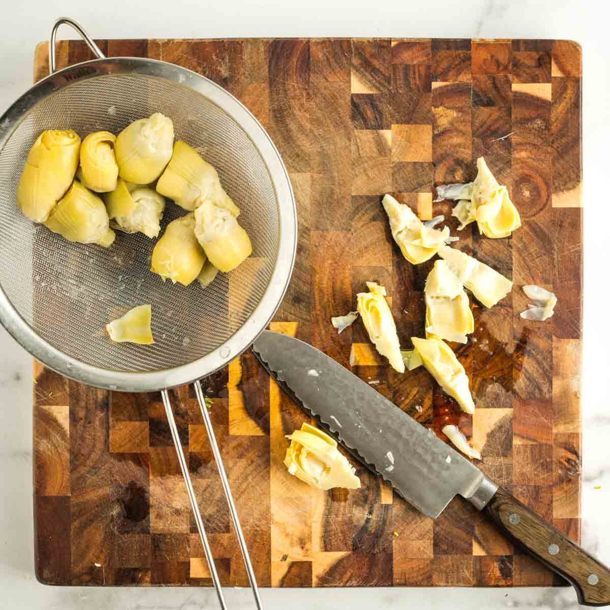 Cutting strained artichoke hearts into quarters on a wooden board. 
