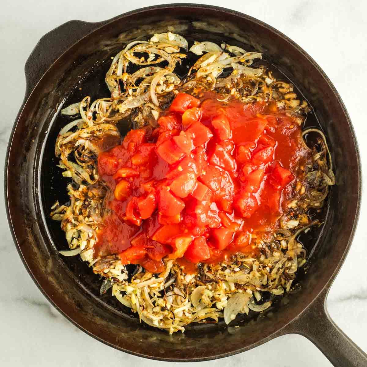 Canned diced tomatoes on top of caramelized onions and spices in a cast iron skillet.