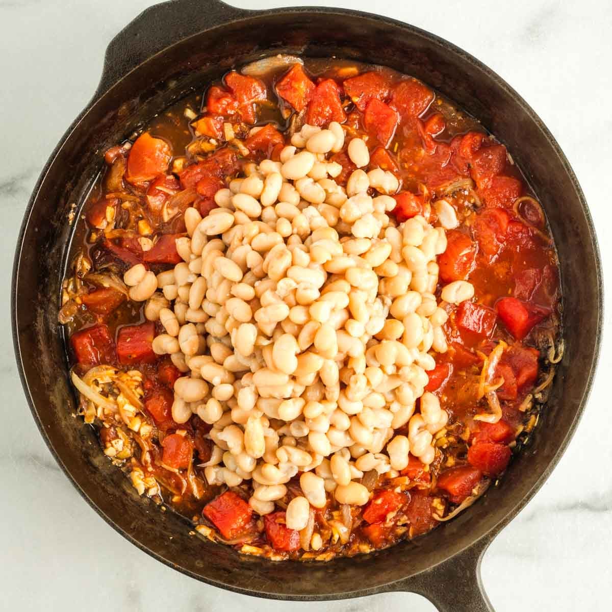 White beans on top of a tomato and onion mixture in a cast iron skillet. 
