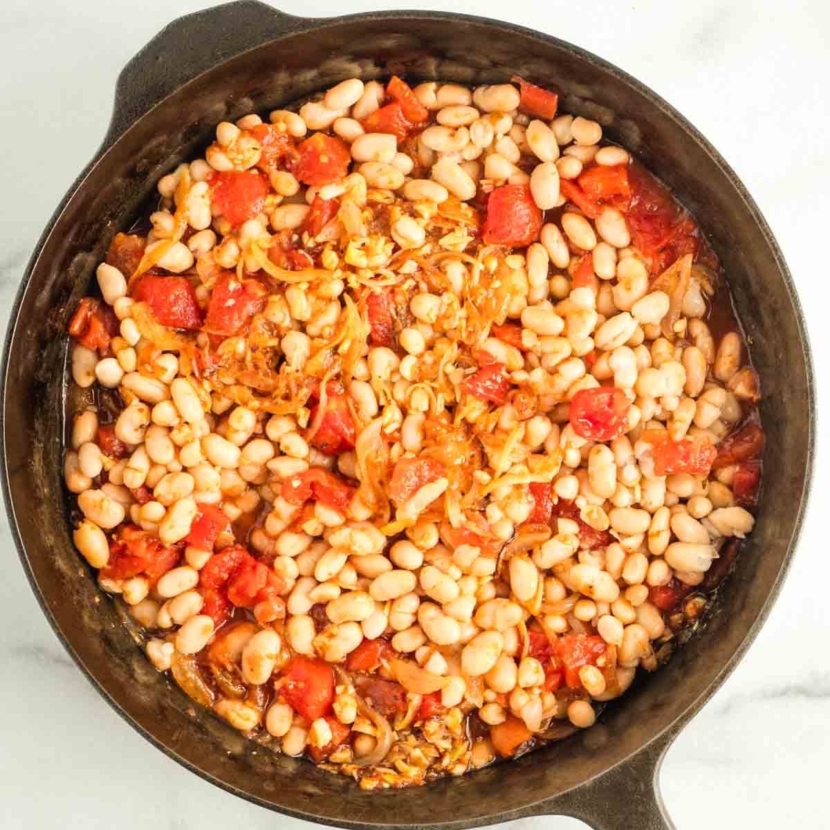 White beans, onions and tomatoes in a skillet.