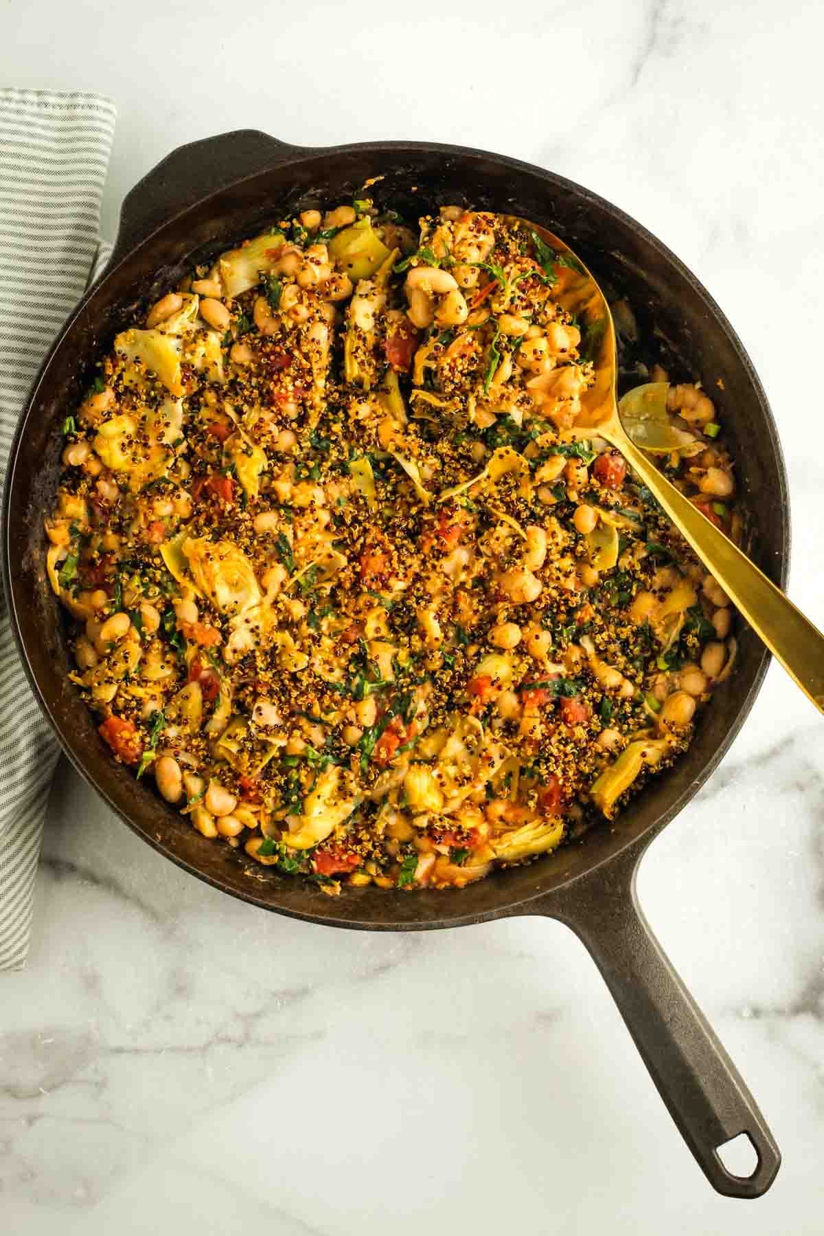 Gold spoon scooping up some crispy quinoa topped lemony tuscan white bean and tomato skillet dinner. 