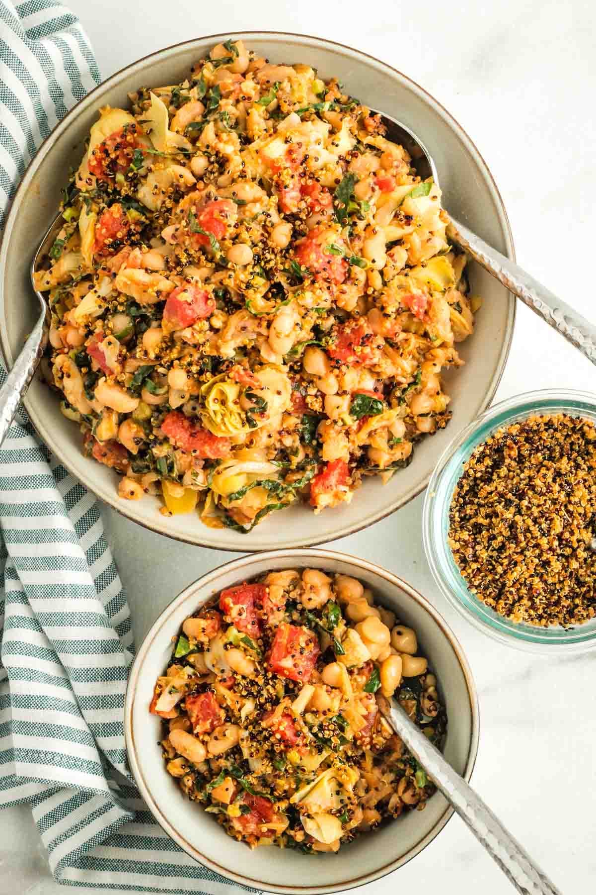 Bowl of Tuscan white bean, tomato and artichoke heart dinner with crispy quinoa topping to spoon on top. 